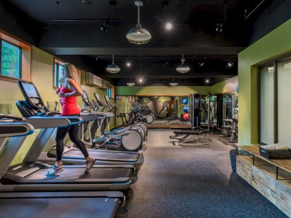 A woman exercises on a treadmill in a spacious gym with various fitness equipment and mirrors on the walls.