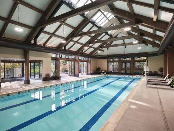 An indoor swimming pool with large windows, lounge chairs, and a high ceiling with exposed beams.