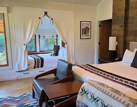 A modern bedroom with two beds, wooden accents, patterned blankets, and big windows overlooking lush greenery.
