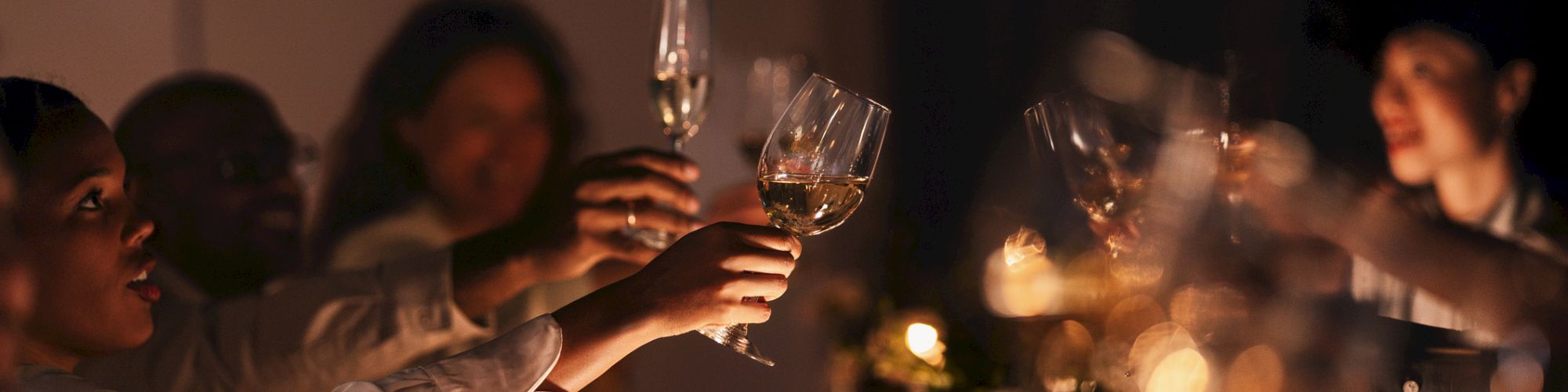Friends clink champagne glasses at a candlelit celebration, toasting together in warm golden light.