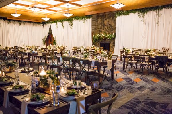 A decorated banquet hall with tables set for an event, featuring greenery, candles, and elegant table settings.
