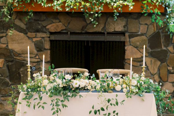 A decorated fireplace with greenery and a white table adorned with foliage and candles in a cozy setting.