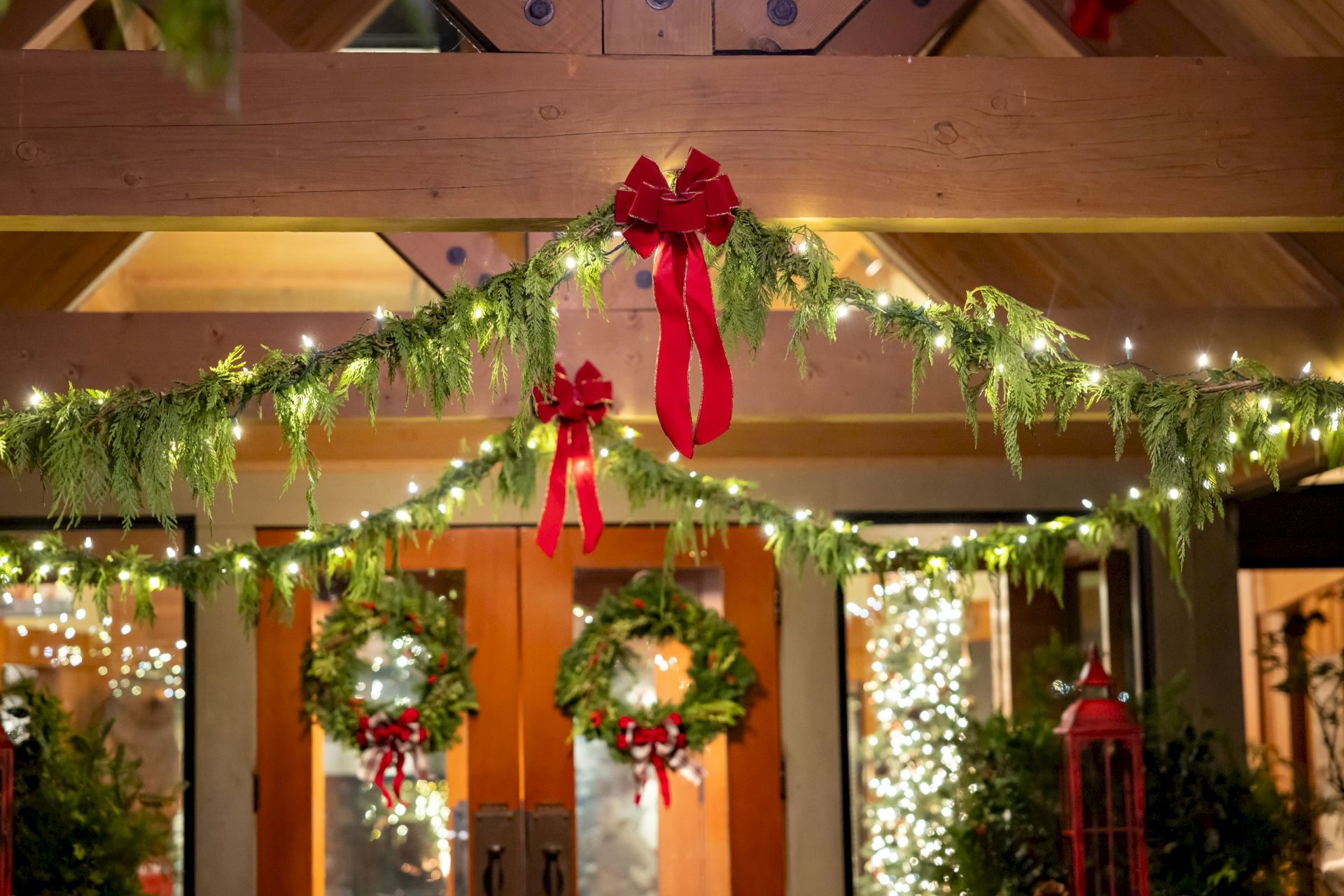 A Christmas garland indoors with twinkling lights and a big red bow creates a festive holiday display.