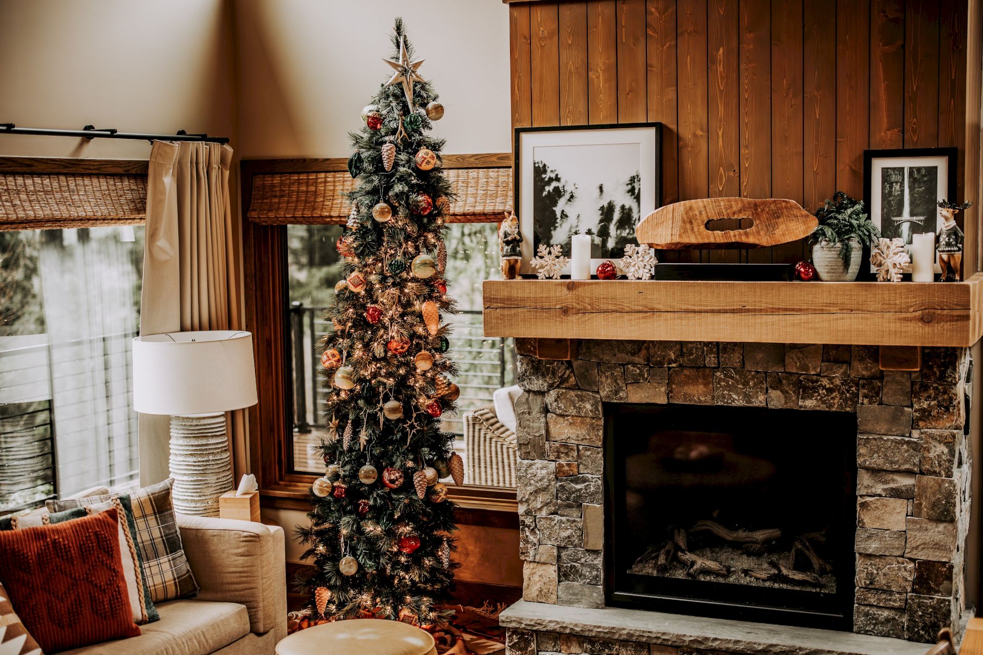 A cozy living room features a decorated Christmas tree, a stone fireplace with candles and ornaments, and warm holiday decor.