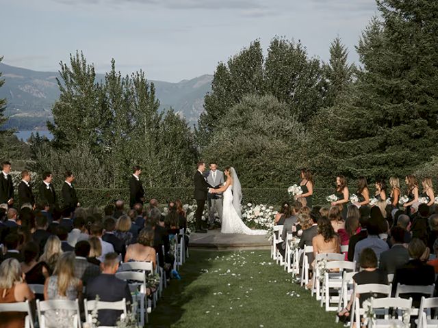 A wedding ceremony with a couple getting married outdoors, surrounded by guests seated on white chairs, and a scenic backdrop.