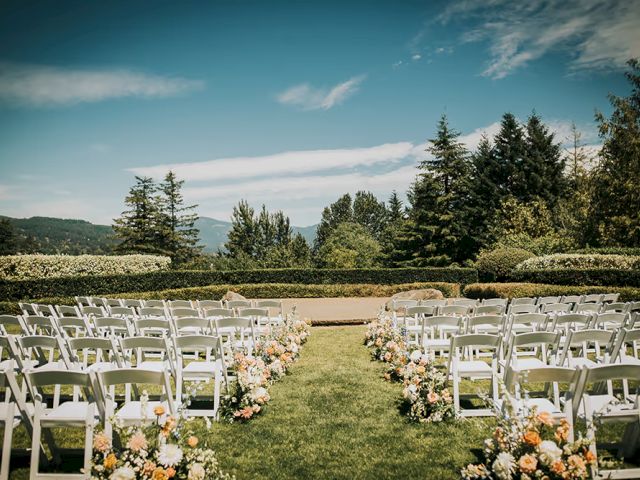 Outdoor wedding setup with white chairs and floral arrangements, overlooking a scenic view of trees and mountains, under a clear blue sky.