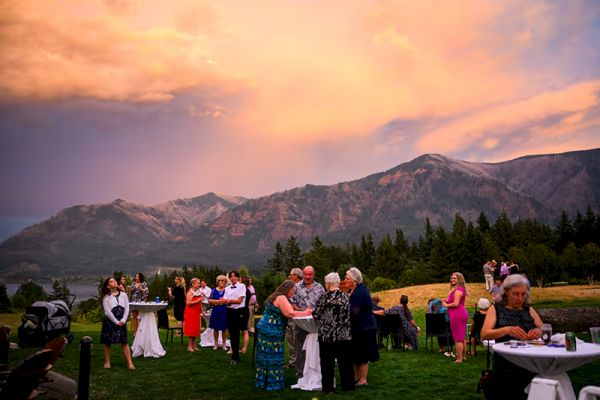A group of people at an outdoor event with mountains in the background under a colorful sky.