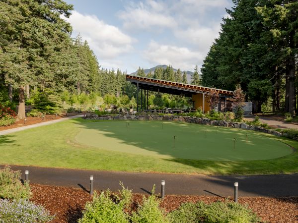 A landscaped area with a putting green, surrounded by trees and a modern canopy structure in the background.