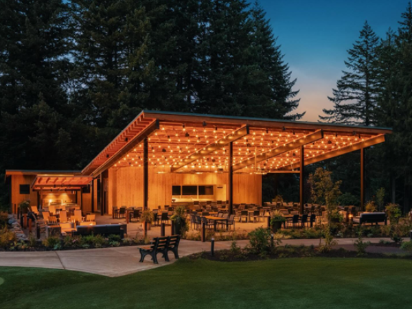 An outdoor pavilion with string lights, tables, and seating, surrounded by trees in a serene setting during twilight.