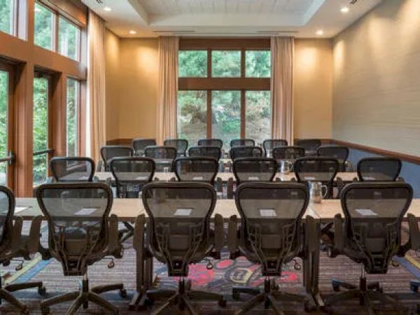 A conference room with tables, chairs, and natural light from large windows, set for a meeting with chairs facing the front.