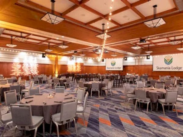 The image shows a large, elegantly set banquet hall with round tables, chairs, and warm lighting, featuring "Suaramia Lodge" banners.