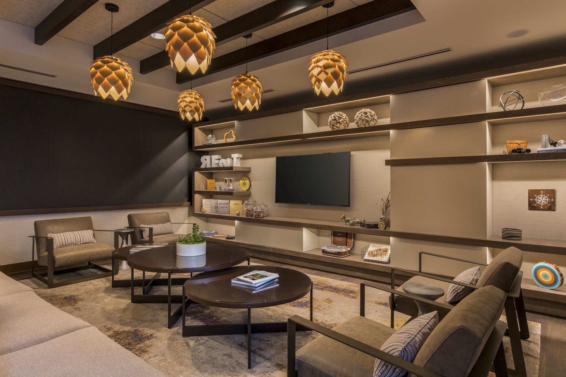 A cozy living room with modern furniture, decorated shelves, a TV, and unique pendant lights hanging from the ceiling.