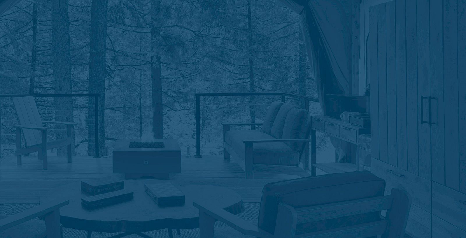 A cozy outdoor seating area with chairs and a table overlooks a forest, giving a serene nature vibe.