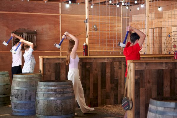 People are participating in an indoor axe-throwing activity, aiming at wooden targets in an enclosed area.