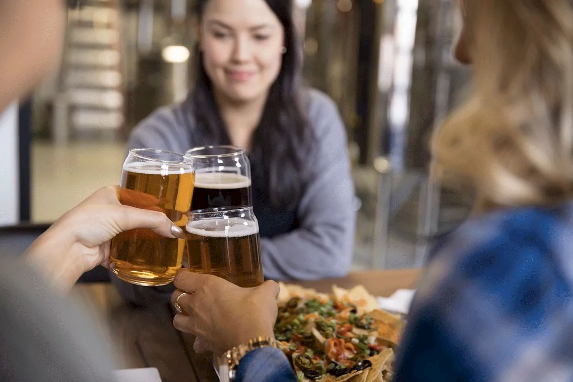 People toasting with beer glasses at a table, enjoying drinks and food together in a social setting.