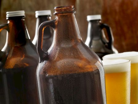 Brown beer growlers and glasses filled with light beer on a wooden table, with condensation visible, in a cozy setting.
