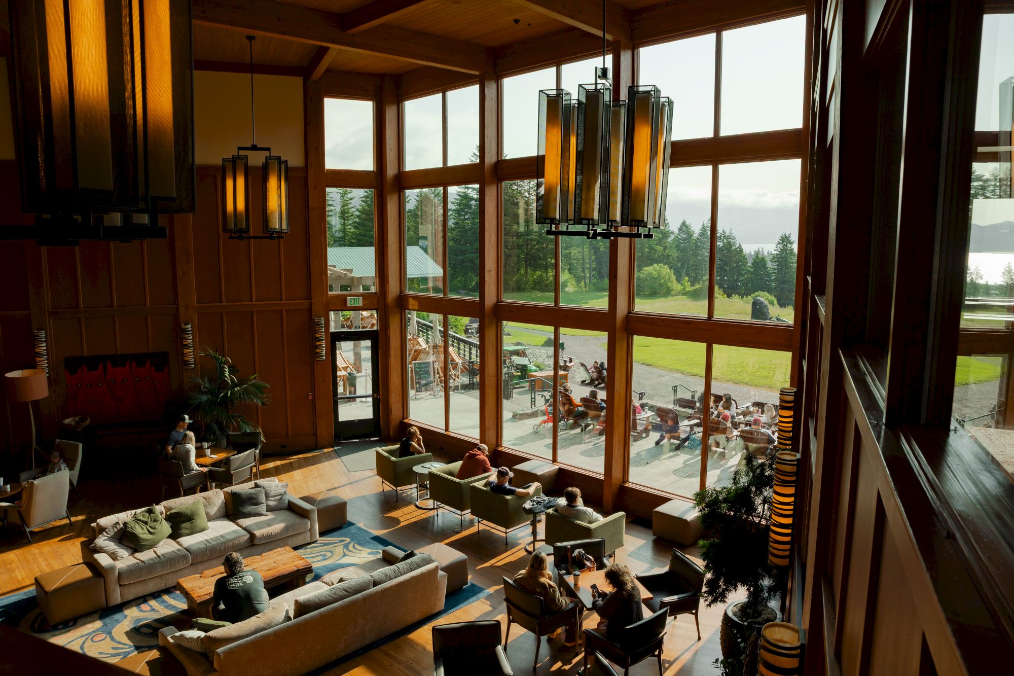 A spacious, elegant lounge area with large windows, comfortable seating, and people relaxing, offering a scenic view of greenery and water outside.