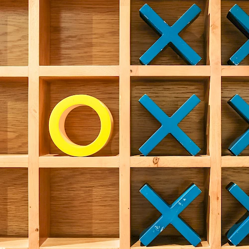 A wooden tic-tac-toe grid with blue Xs and one yellow O, forming a few Xs across but no clear winning line.
