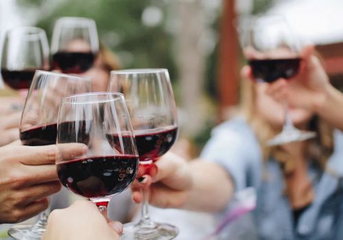 People raising glasses of red wine in a toast, possibly celebrating or enjoying a gathering outdoors.