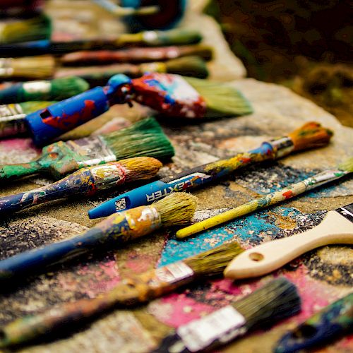 The image shows a collection of paintbrushes with colorful paint on a surface, arranged in an artistic manner.