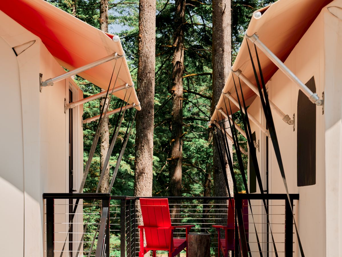 The image shows a wooden deck between two tent-like structures in a forest setting, featuring a red chair.