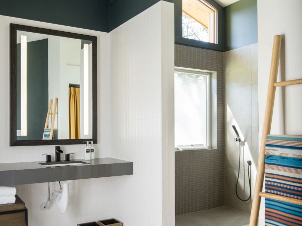 A modern bathroom features a sink with a mirror, walk-in shower, and ladder-style towel rack, with towels hanging.