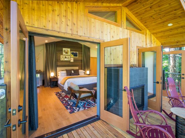 A serene cabin features an inviting bedroom with a large bed, a cozy porch with chairs, and lush greenery surrounding the space.