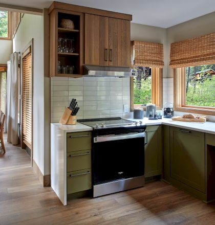 A modern kitchen with wooden cabinets, stainless steel appliances, and large windows overlooking greenery.