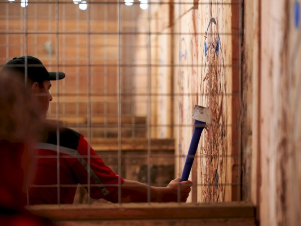 The image shows a person in a cage-like area throwing an axe at a wooden target on the wall.