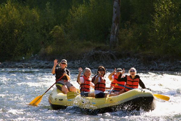A group of people is rafting on a river, wearing life jackets and paddling, while water splashes around them.