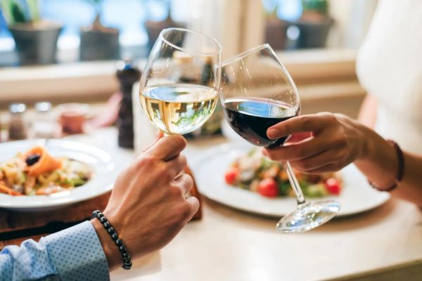 Two people clinking wine glasses over a table with plates of food, creating a celebratory or romantic atmosphere.