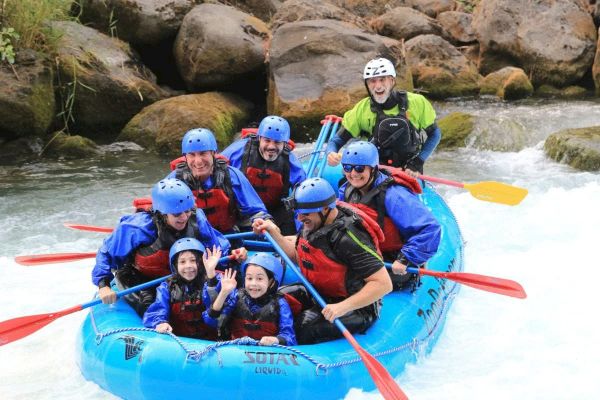 A group of people wearing helmets and life jackets are white-water rafting on a river, looking excited and cheerful while paddling.
