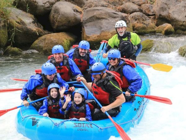 A group of people wearing helmets and life jackets are white-water rafting on a river, looking excited and cheerful while paddling.