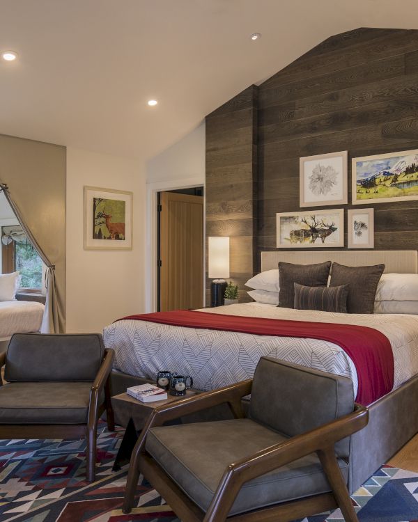 A cozy bedroom features a large bed, armchairs, rustic decor, and a window seat with cushions, all in a warm, inviting ambiance.