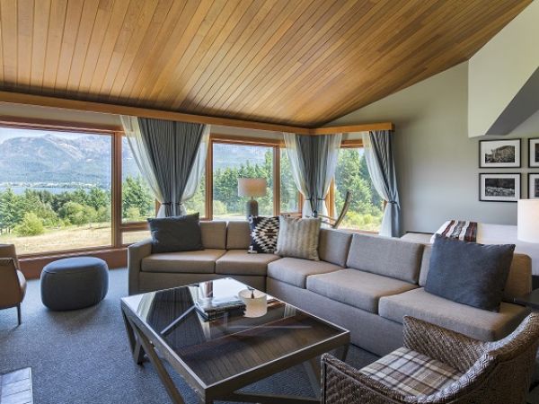 A cozy living room with a large sofa, a coffee table, and panoramic windows offering a scenic mountain and forest view, decorated tastefully.