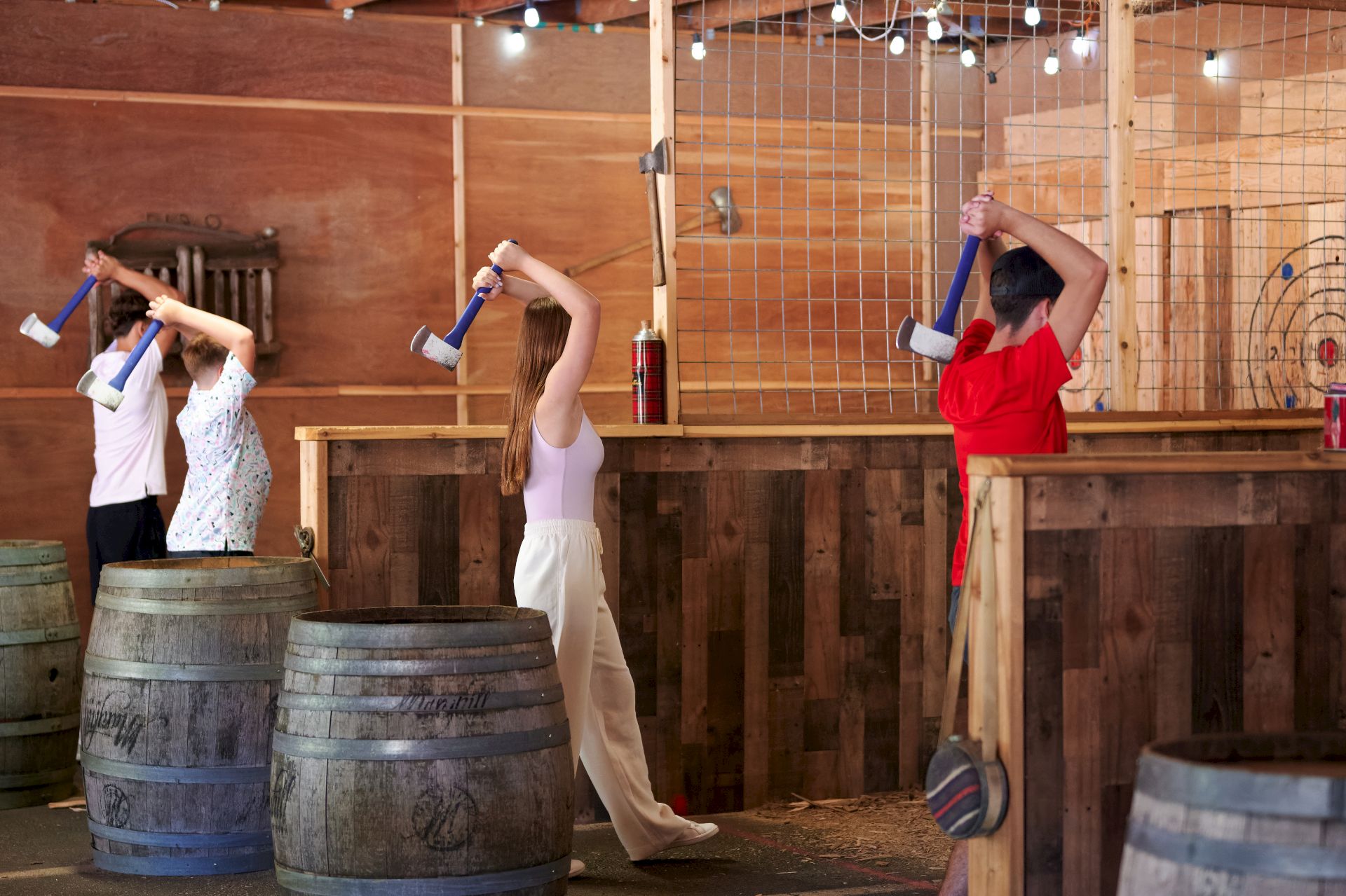 People are participating in an axe-throwing activity indoors, aiming at targets on wooden boards.