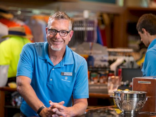A smiling person in a blue polo stands in a shop with another person, surrounded by clothing and merchandise.