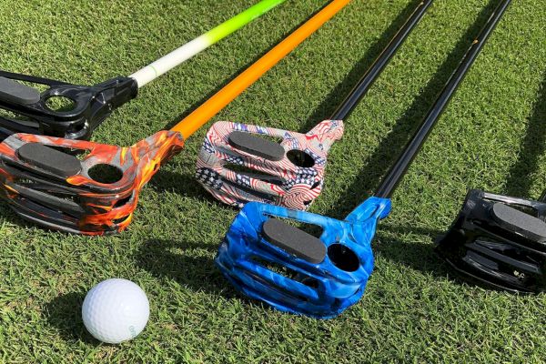 Various colorful golf putters with camouflage patterns are lying on grass next to a golf ball.