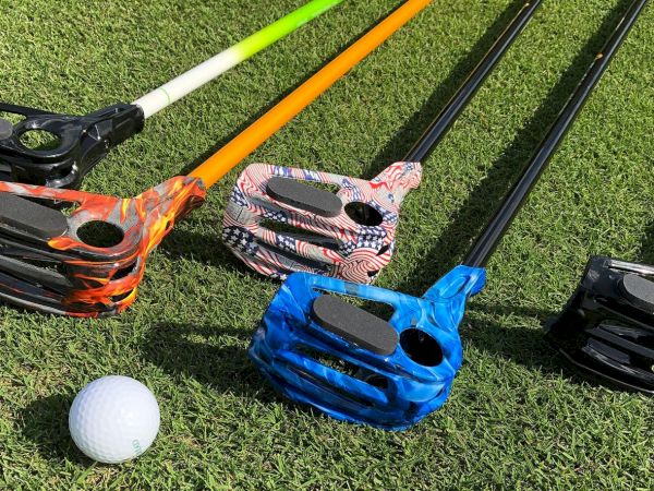 Various colorful golf putters with camouflage patterns are lying on grass next to a golf ball.