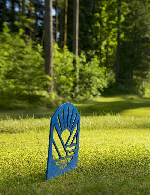 A blue, hand-shaped sign on a grassy fairway with trees lining a sunny golf course in the background.