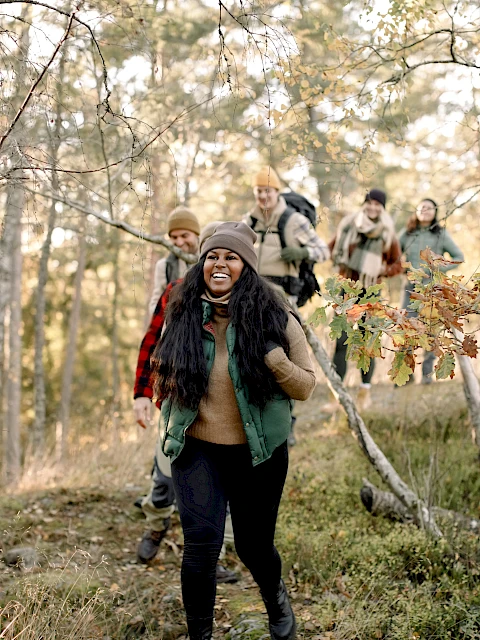 A group of people hiking through a forested area with smiles, dressed in casual outdoor clothing, enjoying the natural surroundings.