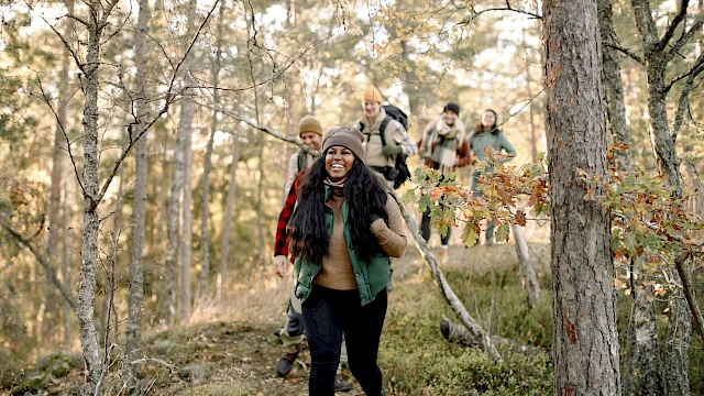 A group of people hiking through a forested area with smiles, dressed in casual outdoor clothing, enjoying the natural surroundings.