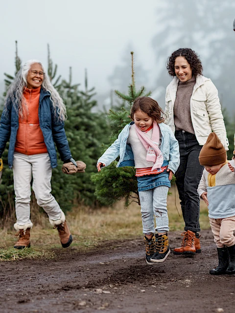 A family of four walks with a child holding hands with adults on a muddy trail in a forest; a joyous outdoor outing.