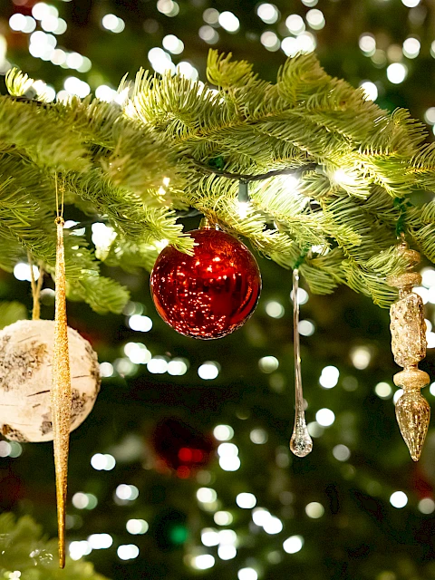 Decorated Christmas tree branches with hanging ornaments, baubles, and twinkling lights creating a festive, luminous scene.