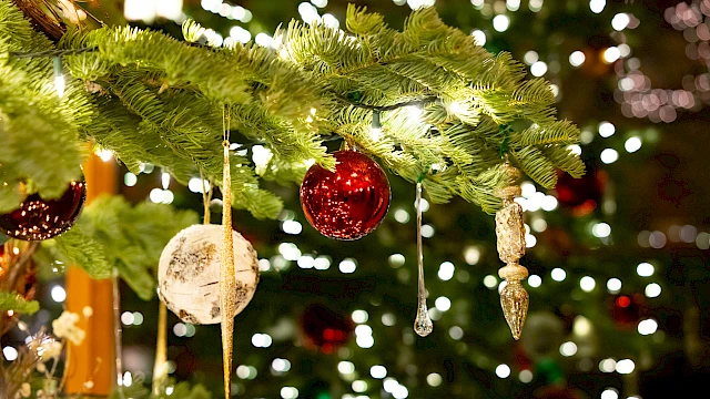 Decorated Christmas tree branches with hanging ornaments, baubles, and twinkling lights creating a festive, luminous scene.