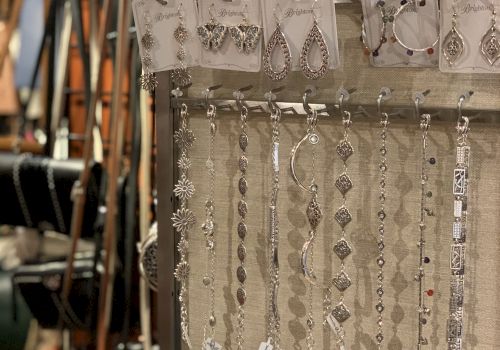 A jewelry display with dangling earrings and bracelets on a rack, silver pieces catching light, shoppers&rsquo; items in a shop.