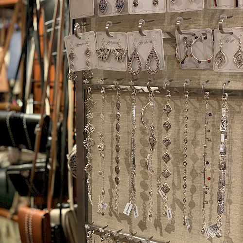 A jewelry display with dangling earrings and bracelets on a rack, silver pieces catching light, shoppers&rsquo; items in a shop.