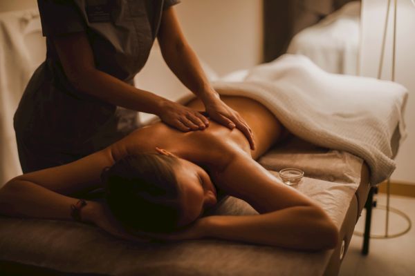 A person receiving a back massage in a dimly lit room, lying on a massage table under a white towel.