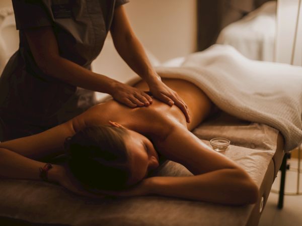 A person receiving a back massage in a dimly lit room, lying on a massage table under a white towel.