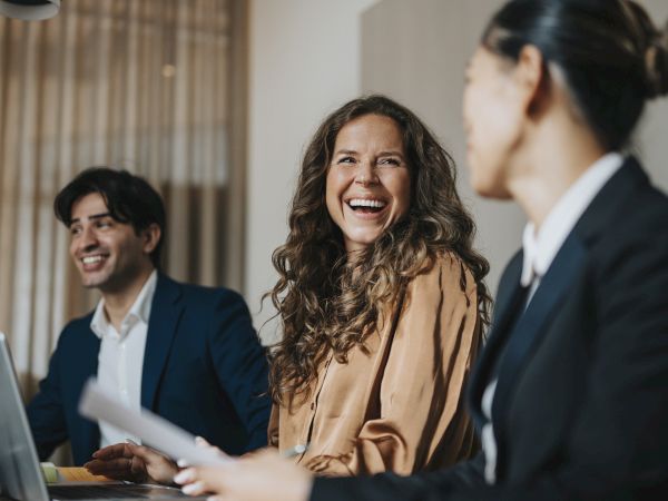 Three people are sitting at a table, smiling and engaged in conversation, suggesting a positive and collaborative environment.